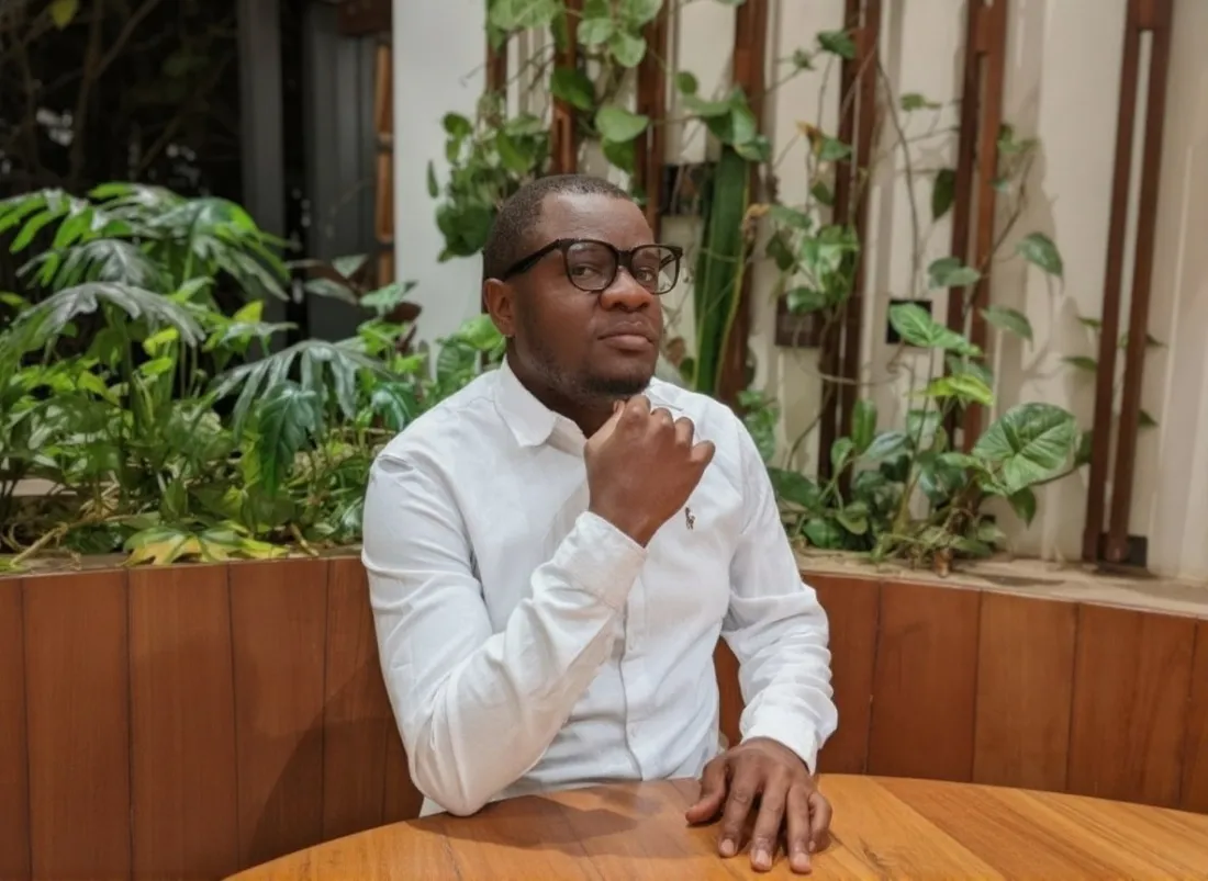 Fokwa Siaka seated at a wooden table in front of green plants